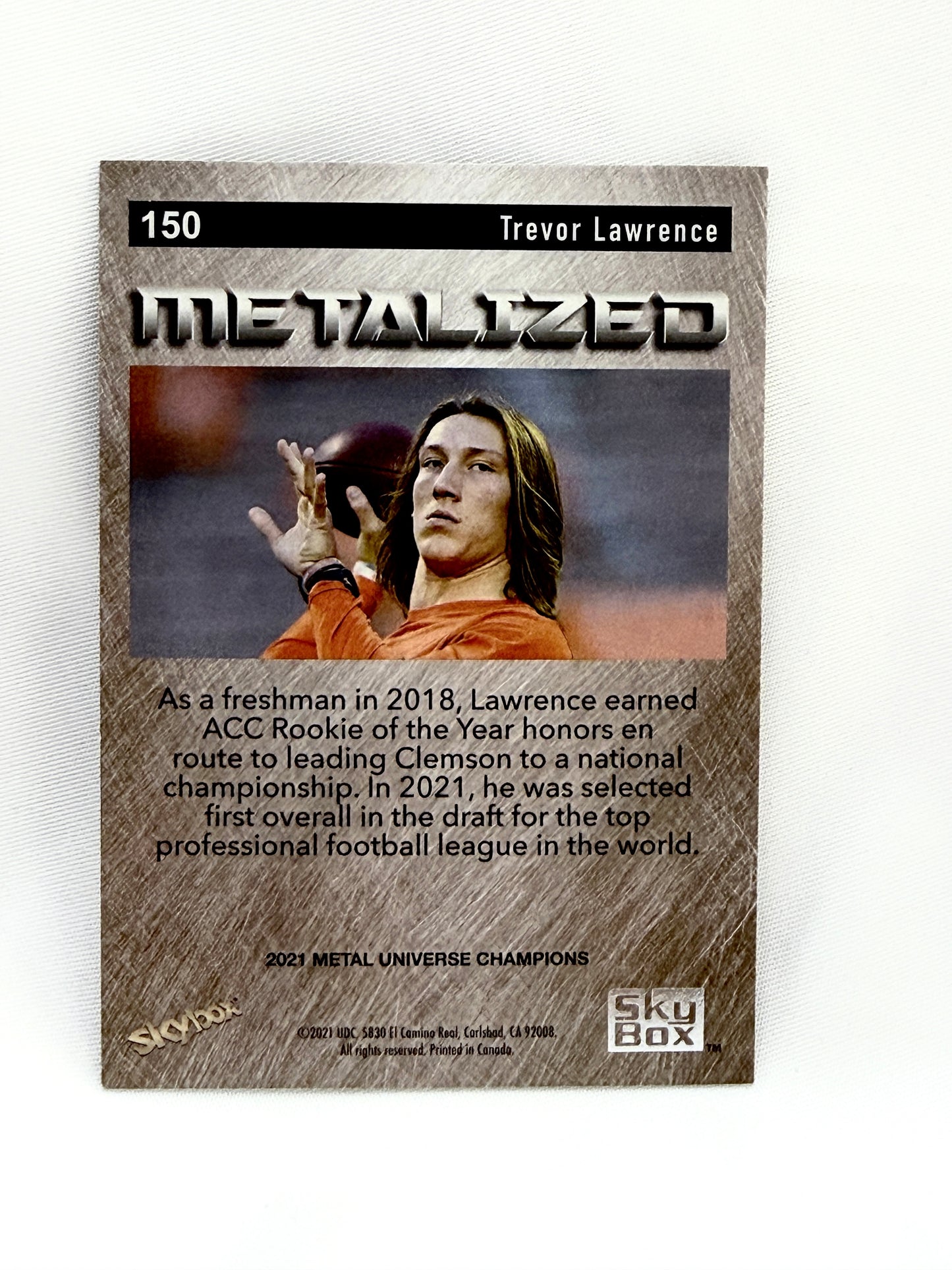 A collectible trading card featuring Trevor Lawrence, with the title 'Metalized' and '2021 Metal Universe Champions' at the bottom, displayed on a textured white background.