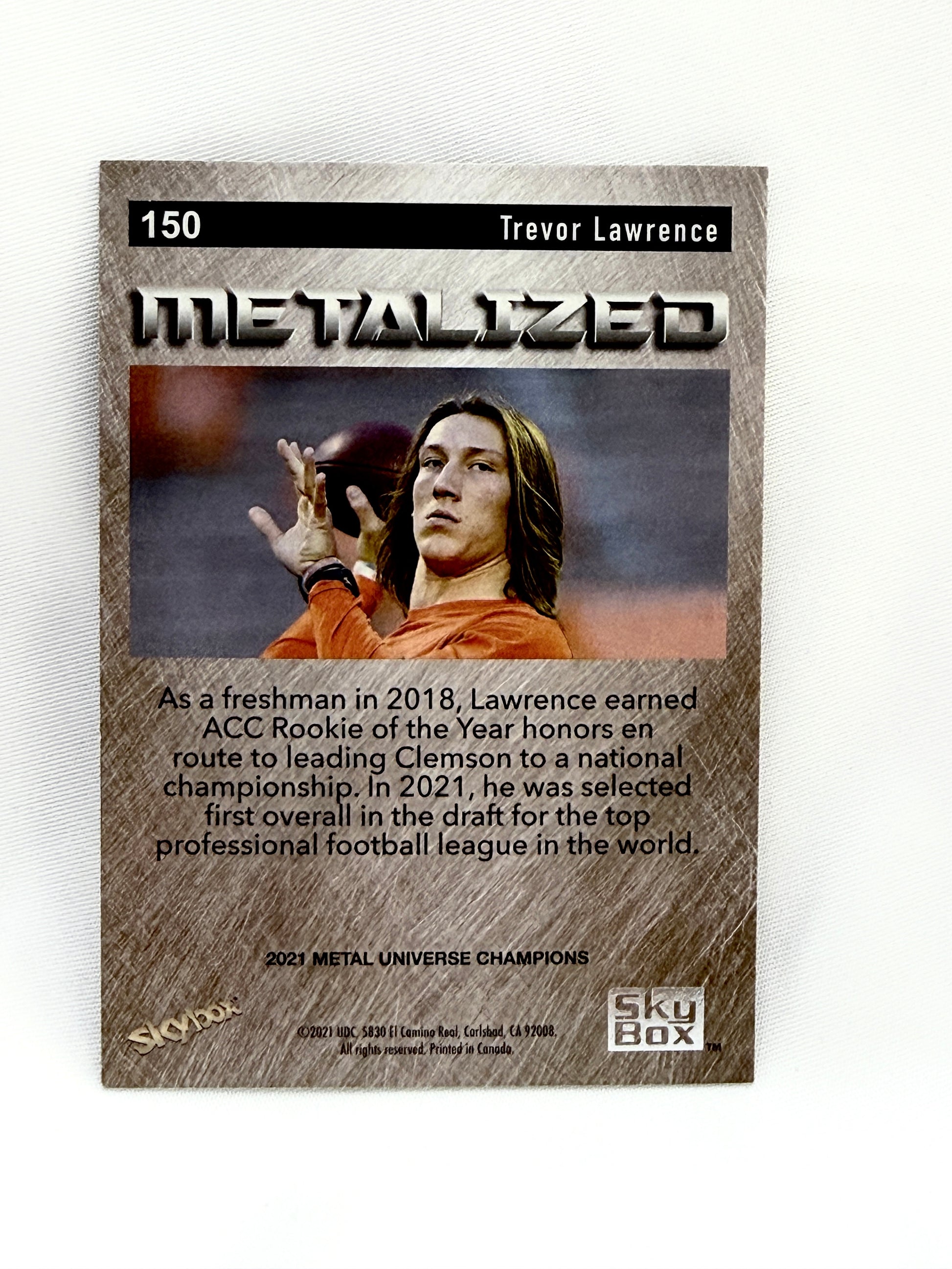A collectible trading card featuring Trevor Lawrence, with the title 'Metalized' and '2021 Metal Universe Champions' at the bottom, displayed on a textured white background.