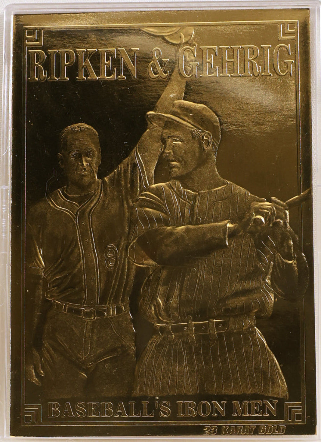 A rectangular bronze-toned commemorative plaque featuring two baseball players, with raised text reading 'RIPKEN & GEHRIG' at the top and 'BASEBALL'S IRON MEN' at the bottom. The plaque is displayed in a clear plastic protective case against a light neutral background.