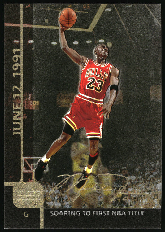 A basketball trading card featuring Michael Jordan in a red Chicago Bulls jersey with the number 23, mid-jump and reaching for a basketball. The card includes a gold vertical strip on the left with the date 'JUNE 12, 1991' and text at the bottom reading 'SOARING TO FIRST NBA TITLE'.