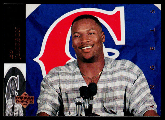 A collectible sports trading card featuring a smiling man in a gray and white plaid shirt standing in front of microphones, with a large blue, red, and white sports logo in the background and a black banner at the bottom.
